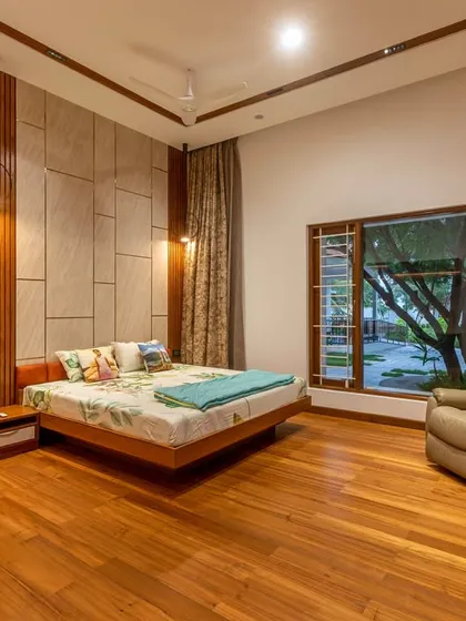 This bedroom features warm wooden flooring and a textured feature wall behind the bed. A large window provides ample natural light and a connection to the landscape.