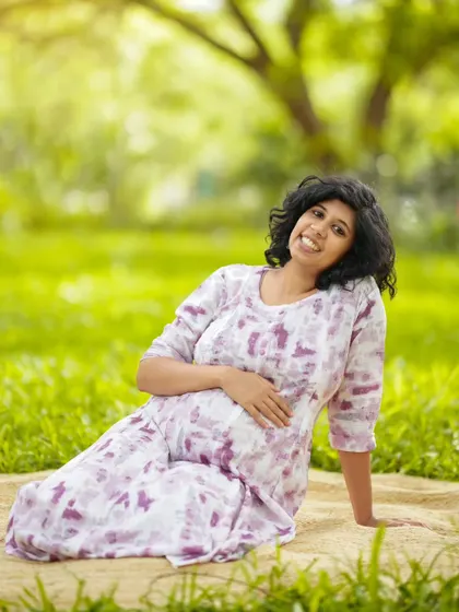 A bright and cheerful solo maternity portrait. The mother-to-be is relaxing on a blanket in a sunny park, wearing a lovely tie-dye print dress.