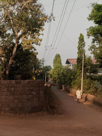 The street view of Maison Rouge, showing how the laterite wall and vernacular form blend into the rural Konkan landscape.