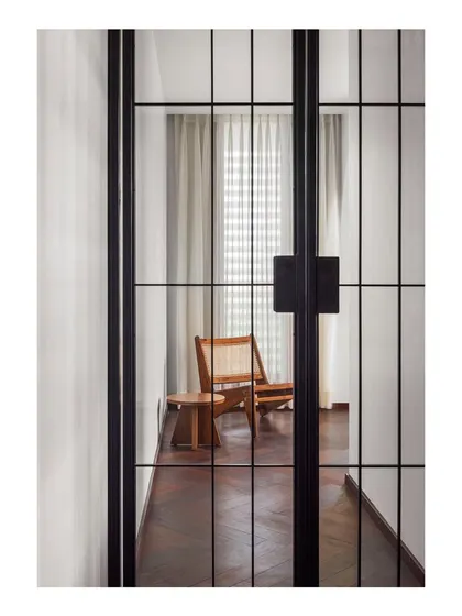 A view through a full-height, metal-grid pivot door into a quiet lounge space. I use internal doors and screens like this to create visual interest and define zones without closing them off completely.