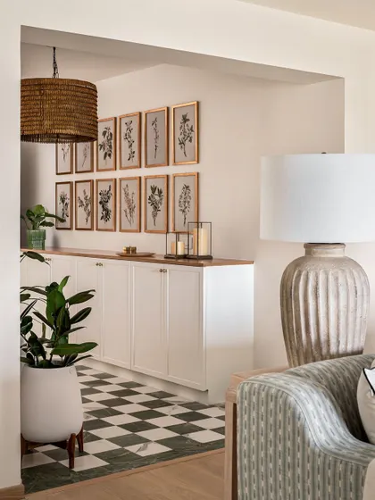 A view from the living room into the foyer, where a long console provides ample storage. The gallery wall of botanical prints and a large woven pendant light introduce the home's modern coastal theme.