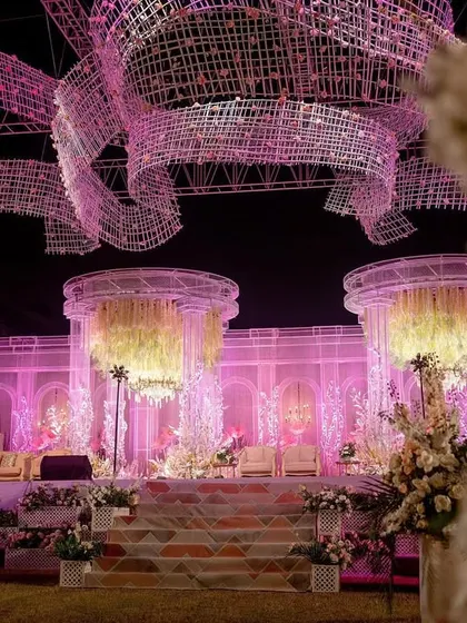 A beautiful perspective of the stage, framed by floral arrangements in the foreground. The layers of design, from the floor decor to the stage and the overhead canopy, create a truly immersive visual experience.
