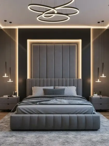 This design features a bold, contemporary aesthetic with a floor-to-ceiling upholstered headboard framed by dramatic backlighting. The monochromatic grey palette and modern lighting fixtures create a sleek and sophisticated look.