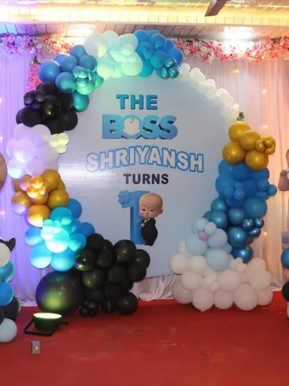 A complete Boss Baby first birthday stage setup with a large backdrop, balloon arch, and multiple character cutouts on balloon pillars.