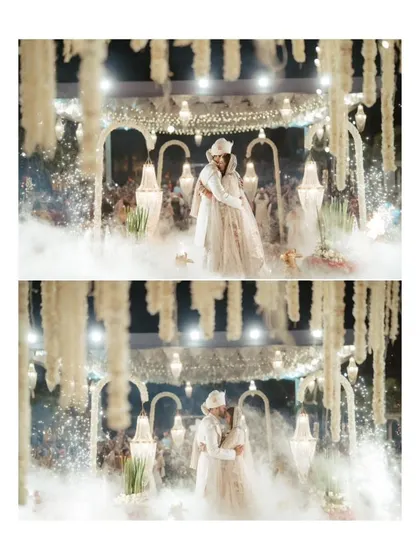 A romantic embrace on the wedding stage, surrounded by smoke and hanging floral arrangements, creating a magical, cinematic moment.