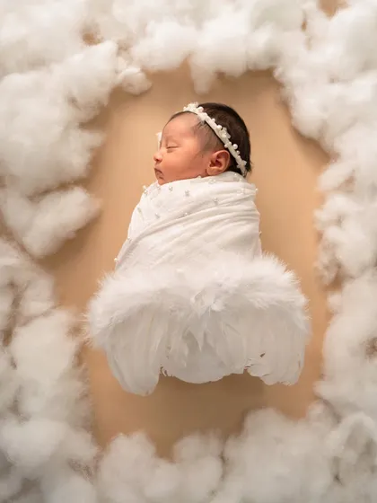 Swaddled with angel wings, this newborn looks serene and peaceful, floating in a frame of soft white clouds.