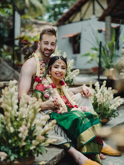 A cross-cultural couple shares a smile, seated on the stone steps of the kalyani. The floral arrangements add to the celebratory and romantic feel.