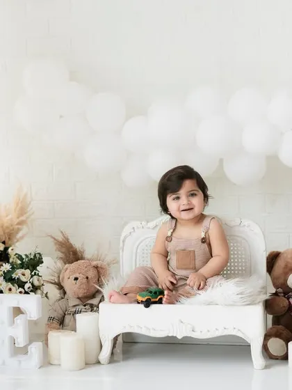 A happy one-year-old on his little white bench. We use classic props that keep the focus on the baby while adding a touch of elegance to the birthday photos.