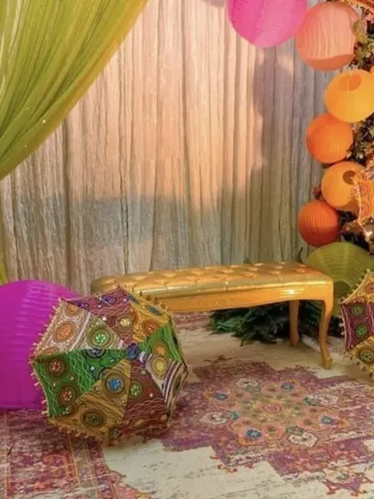 An example of a cozy and colorful Mehndi corner that can be set up at home. The decor uses Rajasthani umbrellas, paper lanterns, and a traditional rug to create a festive and intimate space.