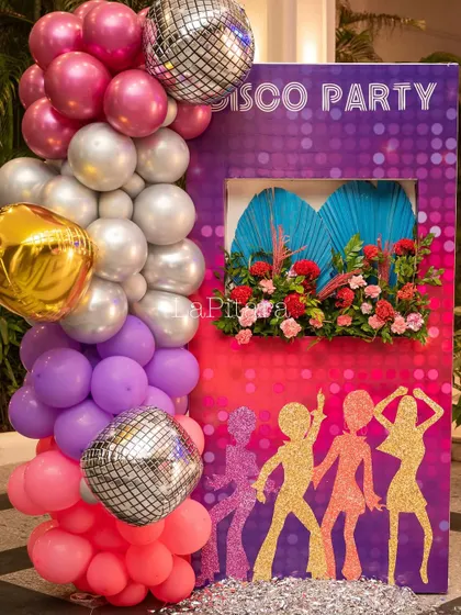 A fun photo-in-hole board with disco dancer silhouettes, decorated with a colorful balloon garland and disco balls.