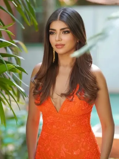 The orange gown pictured in a lush, green environment, proving it's a versatile piece for both indoor and outdoor events.