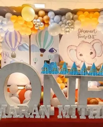 A first birthday party with an elephant and hot air balloon theme, featuring large 'ONE' letters and a custom backdrop.