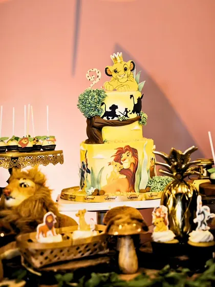 A magnificent Lion King themed dessert table, featuring a detailed two-tier cake, character cupcakes, and jungle-inspired elements like plush lions and golden pineapples.