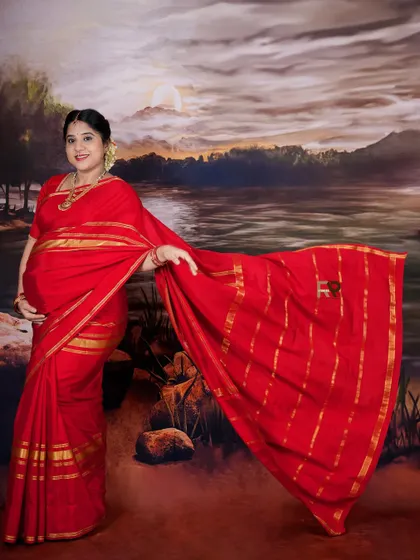 This pose beautifully showcases the intricate details and flow of the red silk saree. The painted landscape backdrop adds a classic, artistic feel to the portrait.