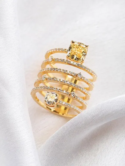 A stunning multi-layered ring with a yellow diamond, shot on a clean white fabric. The simplicity of the styling emphasizes the ring's intricate design and brilliant sparkle.