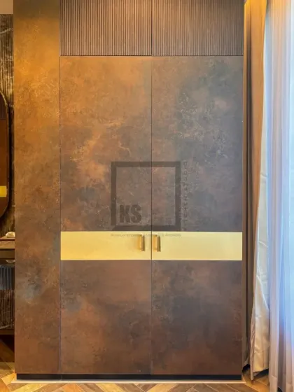 This shot highlights the floor-to-ceiling wardrobe with its unique metallic-finish laminate and fluted wood panel at the top. The horizontal gold handle is not just hardware; it's a central design element.