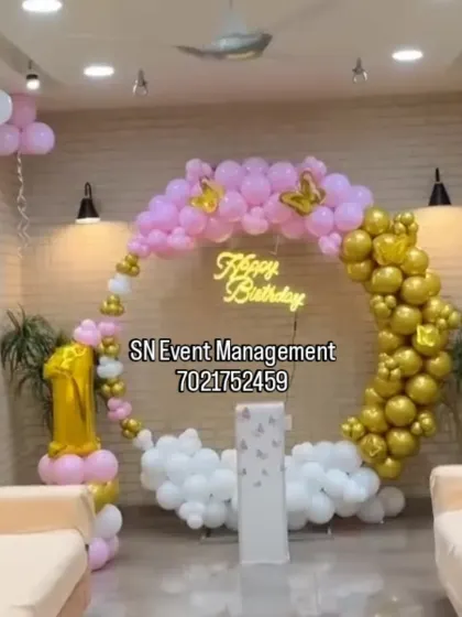 An elegant first birthday decoration in pink, gold, and white. The balloon ring is decorated with butterfly accents and a neon sign, creating a dreamy "cloud nine" effect.