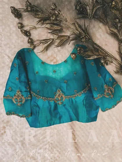 A beautiful teal blue blouse with a sheer yoke and delicate placement embroidery. The design is subtle yet elegant, perfect for a sophisticated look.