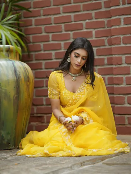A seated pose in the yellow saree, highlighting the delicate embroidery and the beautiful drape.