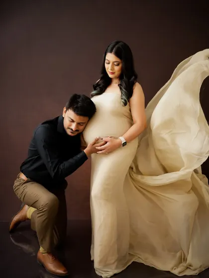 A classic pose filled with love, as the dad-to-be listens to the baby bump. The flowing fabric of the gown adds a touch of elegance to this timeless maternity portrait.