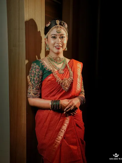 A classic bridal portrait against a dark background, making her vibrant red saree and intricate jewelry stand out.
