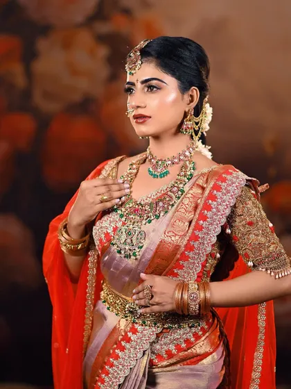 A classic three-quarter portrait of a bride in her full wedding attire. The combination of a light-colored saree with a red veil and heavy gold jewellery creates a stunning contrast.