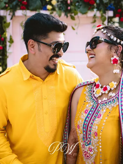 A happy couple, laughing and enjoying their tropical-themed Haldi. Their coordinated yellow outfits and floral jewelry complete the look.
