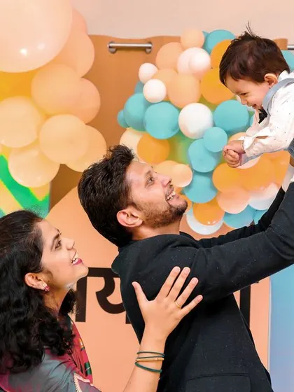 A beautiful family portrait capturing a moment of pure joy. The father lifts his son, and the mother looks on with a smile, all against the backdrop of their custom-designed first birthday party.