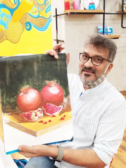 A student holds his realistic still-life painting of pomegranates, showcasing his skill in capturing light, shadow, and texture.
