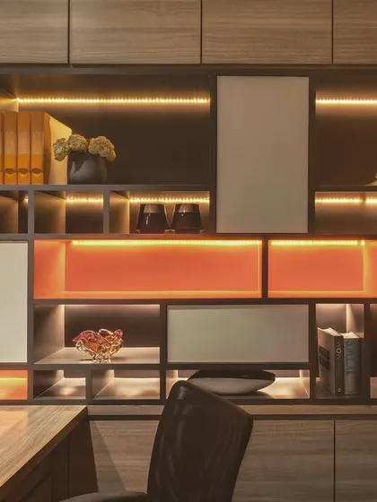 This custom shelving unit in an office demonstrates how to achieve visual harmony. The design balances open and closed sections, with integrated backlighting that highlights decorative objects and adds a warm, ambient glow.