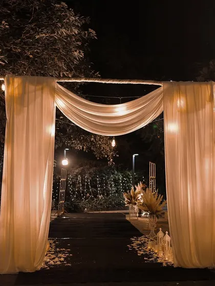A beautifully adorned entry gate, illuminated with string lights to create a warm and inviting ambiance. This rustic-chic design is perfect for setting a festive tone for lawn parties and outdoor celebrations.
