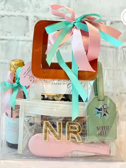 A beach bachelorette hamper in a clear tote, featuring a mini bottle of bubbly, a personalized hairbrush, and a custom luggage tag.