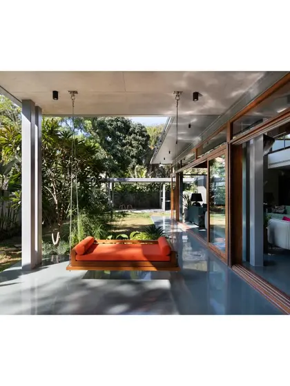 A custom-designed swing on the veranda of the 'House of Canopies'. This space is neither fully inside nor fully outside, offering a sheltered spot to enjoy the garden, embodying the essence of tropical living.