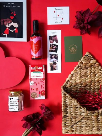 The 'Be Mine Valentine' hamper contents laid out against a red background. This romantic gift includes a framed art print, personalized wine, chocolates, and a photo strip.