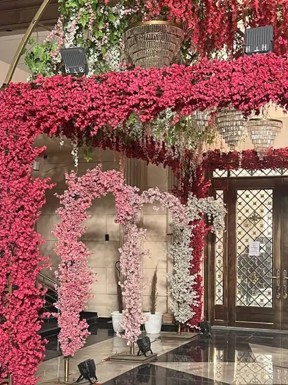 An extravagant entrance decoration for a reception, featuring a dense canopy of red and pink flowers and hanging crystal chandeliers.