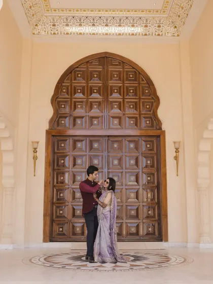 A couple shares a lighthearted moment during their Mehndi at Anantara Jaipur, framed by a grand wooden door.