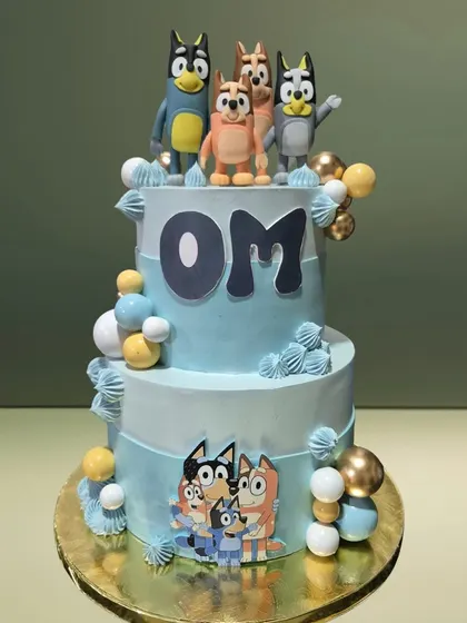 A two-tiered cake celebrating the popular cartoon 'Bluey'. It features the entire Heeler family as toppers and decorations, making it a hit with young fans.