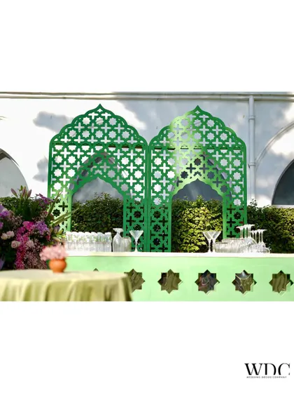 The bar area for the sage green Mehendi. We designed a custom bar with a light green front and a backdrop of darker green jali panels, creating a chic and thematic beverage station.