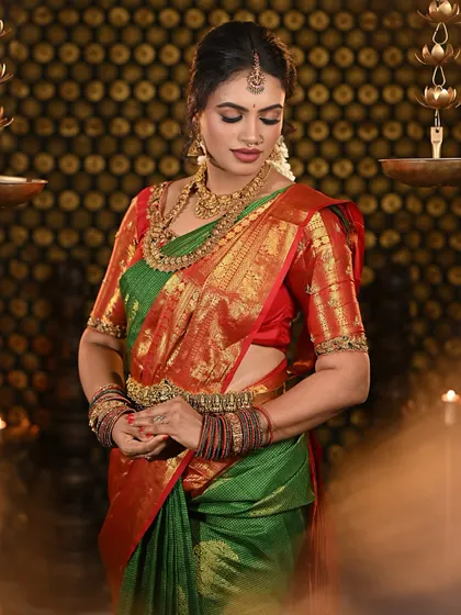 A complete look at a traditional South Indian bride in a stunning green and red Kanjivaram silk saree. The makeup features defined eyes, a bold matte lip, and a flawless base that complements the antique gold jewelry.