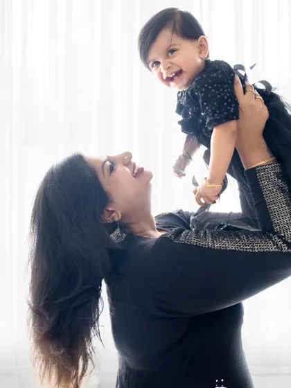A joyful mother lifts her daughter in the air, both of them smiling brightly.