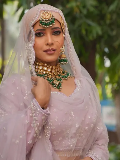 A beautiful Muslim bridal look with a pastel pink outfit and green jewelry. The makeup is soft and elegant.
