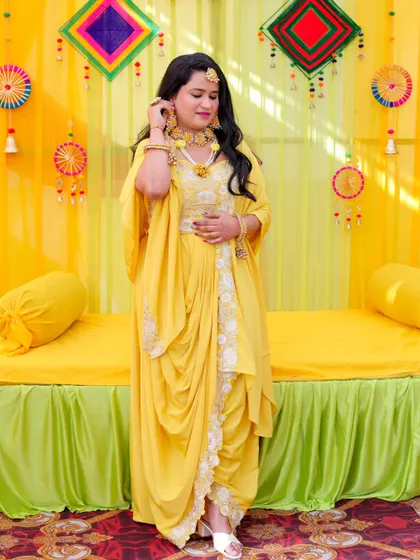 A full-length portrait of the bride in her stylish, modern Haldi outfit. The draped dhoti-style pants and cape are beautifully showcased.
