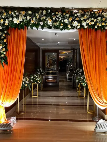 A closer view of the beautifully draped entrance. The combination of the bright orange fabric and the lush white floral arch creates a warm and inviting welcome.