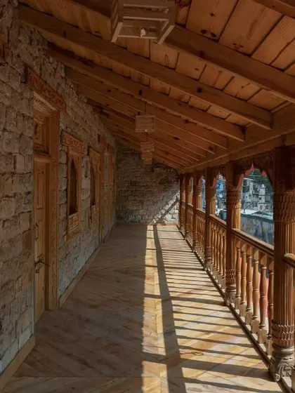 The restored upper floor corridor, where sunlight filters through intricately carved wooden railings, creating a dynamic play of light and shadow along the walkway.