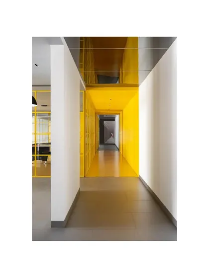 The main corridor of 'The Amber Encase' clubhouse, where a reflective ceiling doubles the height and intensity of the all-yellow space. This immersive design choice turns a simple circulation path into a powerful architectural experience.