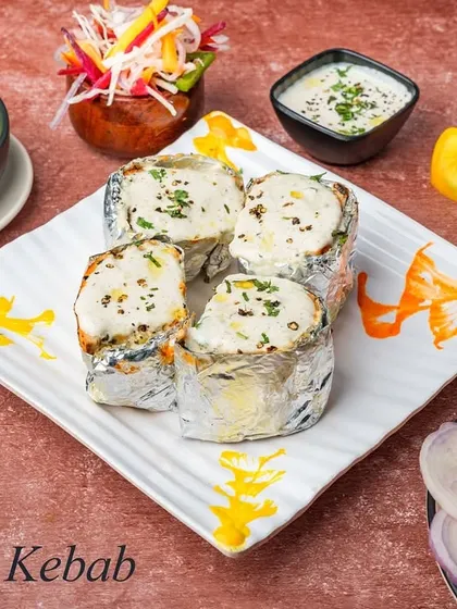 A beautifully plated Moroccan Kebab, showcasing the creamy white sauce and the tender, stuffed chicken pieces wrapped in foil. It's a rich and flavorful dish perfect for a special meal.