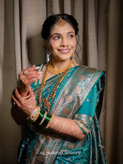 A stunning indoor portrait of the bride in a beautiful teal blue Paithani saree. The makeup is soft and elegant, with a focus on defined eyes and a neutral lip, letting the rich saree color stand out.