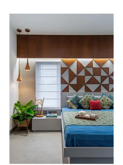 The guest bedroom in "The Far Site House" features a custom-designed headboard with a geometric pattern made of wood and laminate. Pendant lights provide warm, focused light for reading.