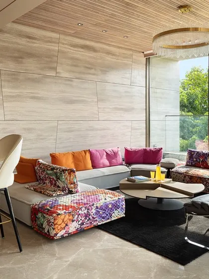 The casual terrace lounge in the Punjabi Bagh residence is designed for relaxation and entertainment. A vibrant Roche Bobois sofa adds a splash of color against the neutral stone walls, overlooking the greenery outside.