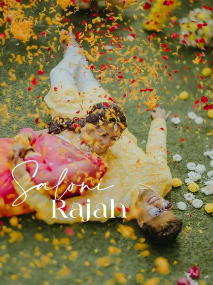A unique aerial shot of the couple lying on the grass, covered in flower petals, capturing a moment of playful romance during their Haldi.